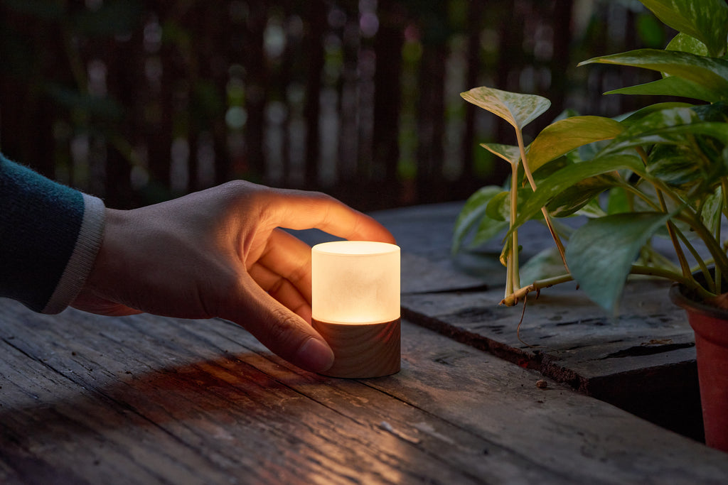 Gingko Design – Lampe Lemelia - Frêne Blanc - 2 Tailles, main posant une petite lampe en bois et verre sur une table