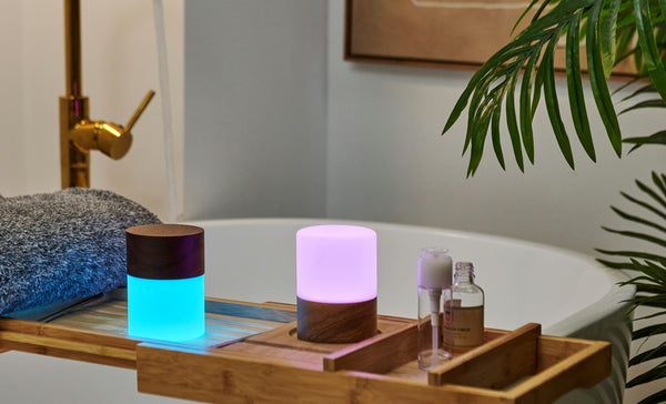 Gingko Design – Lámpara Lemelia - Nogal - 2 Tamaños, dos lámparas ambientales coloridas sobre una estantería de madera en un cuarto de baño