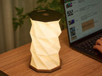 Gingko Design – Luz Twist Hexagon - Nogal Macizo, lámpara de mesa geométrica encendida, colocada sobre un escritorio de madera