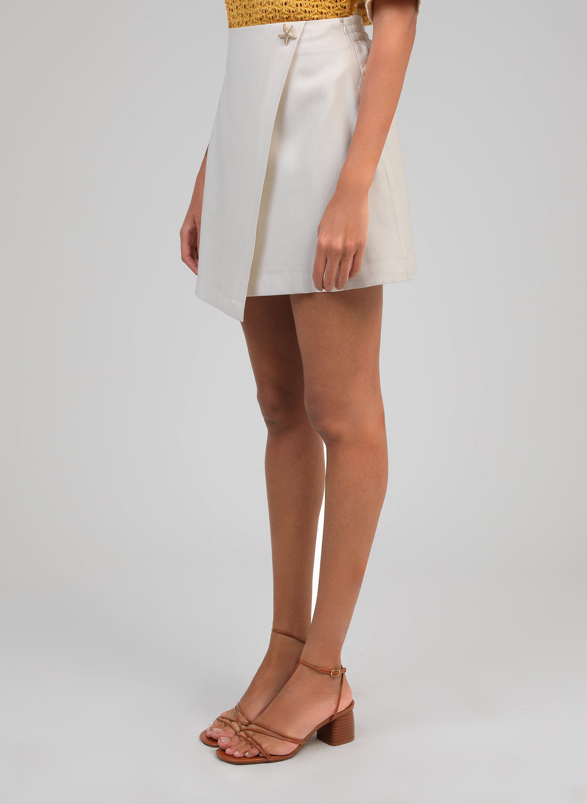 An'ge – Jupe Courte Giovani Ecru, jupe-short portefeuille écrue portée par un mannequin, vue de profil