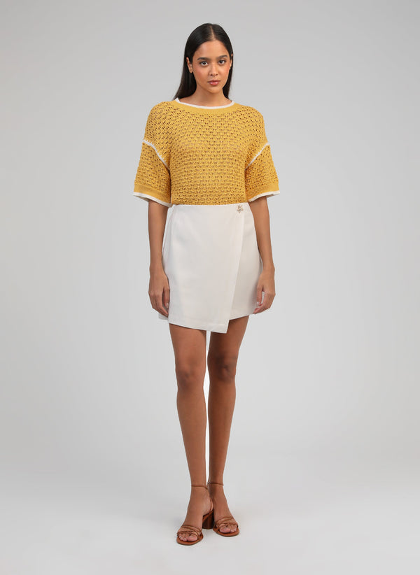 An'ge – Gonna Corta Giovani Ecrù, modella che indossa un maglione giallo in maglia e una gonna bianca
