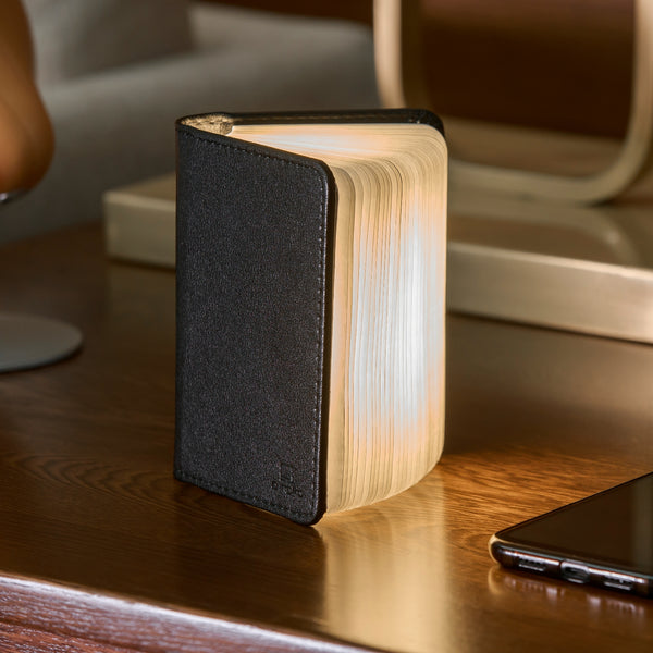 Gingko Design – Lámpara Smart Book LED - Cuero Negro - 2 Tamaños, lámpara libro abierta colocada sobre una mesa de madera