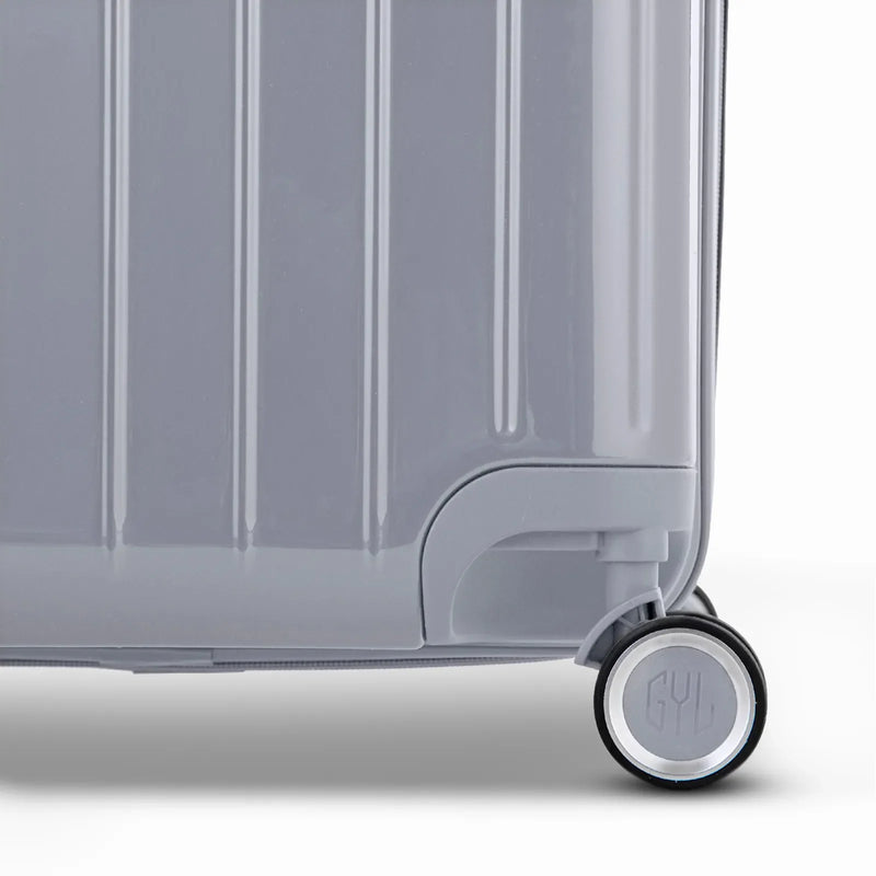 Detalle de la rueda y el logo GYL en el fondo de la maleta baúl de policarbonato plateado brillante. #color_plata