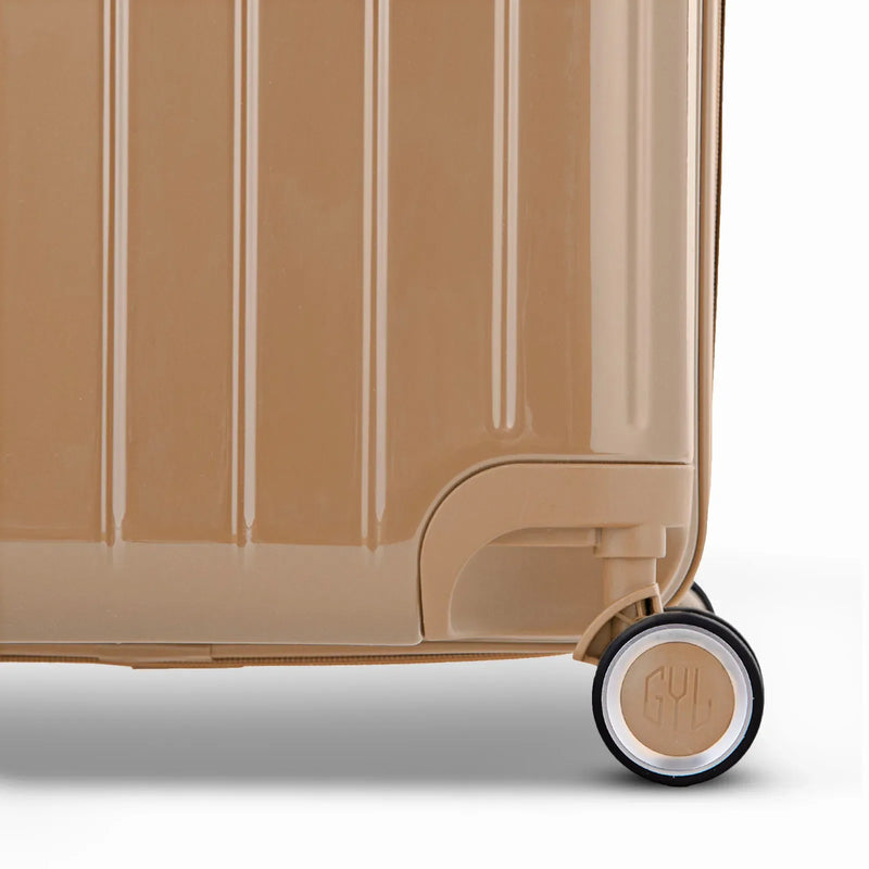 Detalle de la rueda y logo GYL en el fondo de la maleta baúl champagne en policarbonato brillo. #color_champán