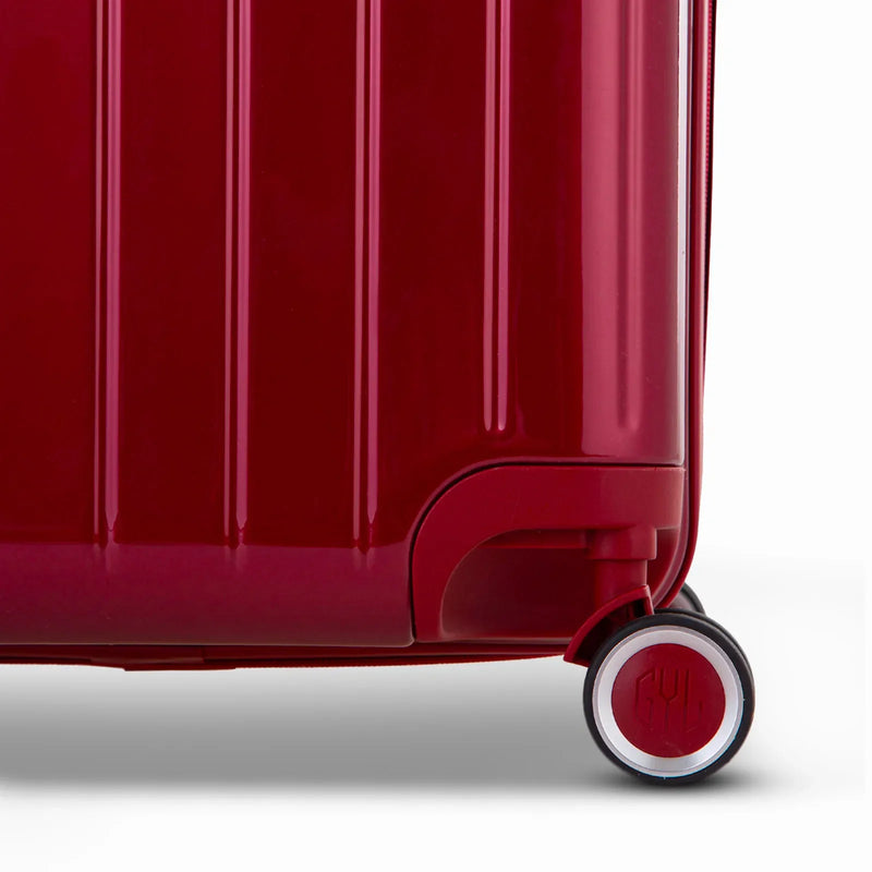 Detalle de la rueda y el logo GYL en el fondo de la maleta baúl rojo oscuro en policarbonato brillo. #color_rojo_oscuro