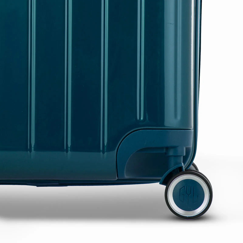 Detalle de la rueda y el logo GYL en el fondo de la maleta baúl de policarbonato brillante. #color_abeto