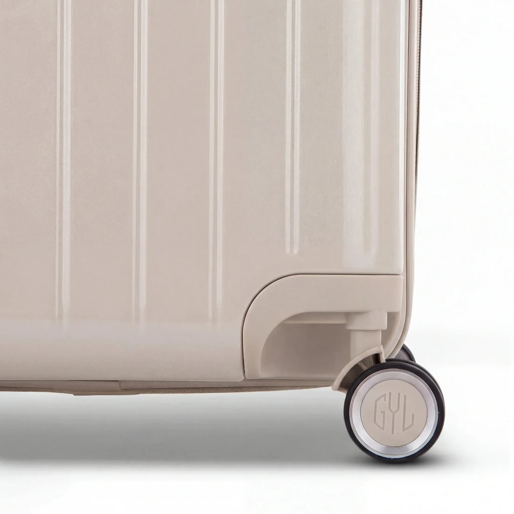 Détail de la roue et du logo GYL sur le bas de la valise trunk nude en polycarbonate brillant. #couleur_nude