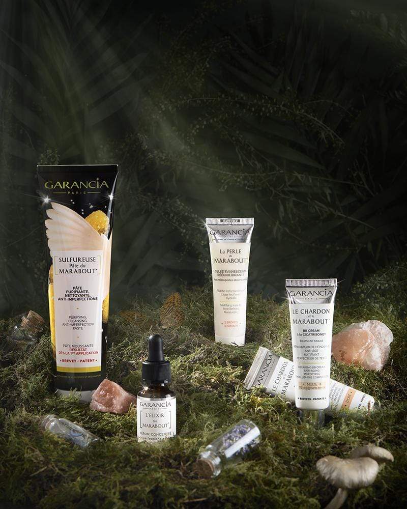 Garancia anti-imperfection care set including Sulfurous Marabout Paste, Marabout Elixir, Marabout Pearl and Thistle and Marabout, staged in a magical undergrowth with moss and crystals.