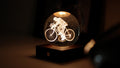 Gingko Design – Amber Crystal-lampa - Cyklist, en lysande glaskula med en graverad cyklist, på en träsockel
