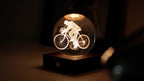 Gingko Design – Amber Crystal-lampa - Cyklist, en lysande glaskula med en graverad cyklist, på en träsockel