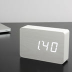 Gingko Design – Brick Click Alarm Clock - White / White LED, light wood digital alarm clock displaying the time on a dark table