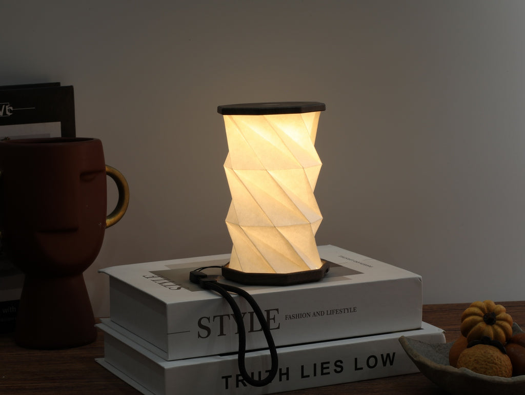 Gingko Design – Leuchte Twist Hexagon – Treibholz-Walnuss – Mini, eingeschaltete faltbare Tischlampe auf Büchern, gemütliche Atmosphäre