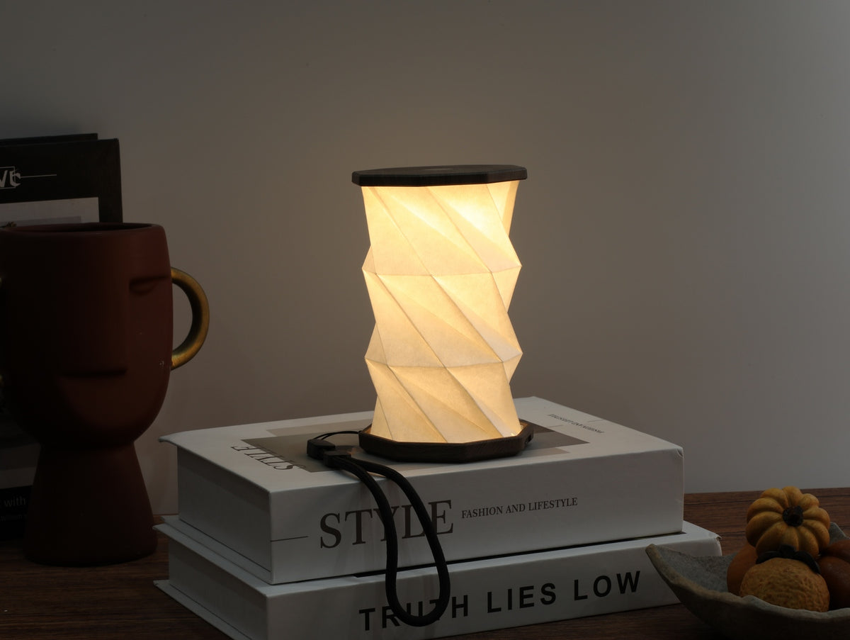 Gingko Design – Leuchte Twist Hexagon – Treibholz-Walnuss – Mini, eingeschaltete faltbare Tischlampe auf Büchern, gemütliche Atmosphäre