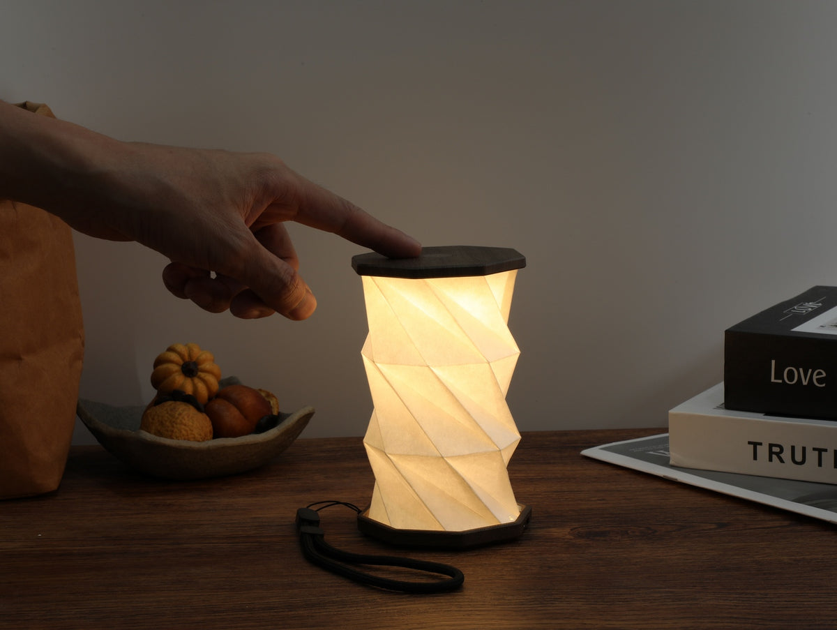 Gingko Design – Leuchte Twist Hexagon – Treibholz-Walnuss – Mini, eingeschaltete faltbare Tischlampe, Hand schaltet sie ein, gemütliche Atmosphäre