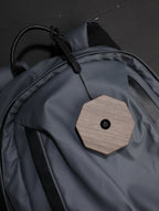 Gingko Design – Twist Hexagon Leuchte - Treibholz Walnuss - Mini, ein achteckiges Objekt aus hellem Holz mit schwarzem Knopf auf einer grauen Tasche