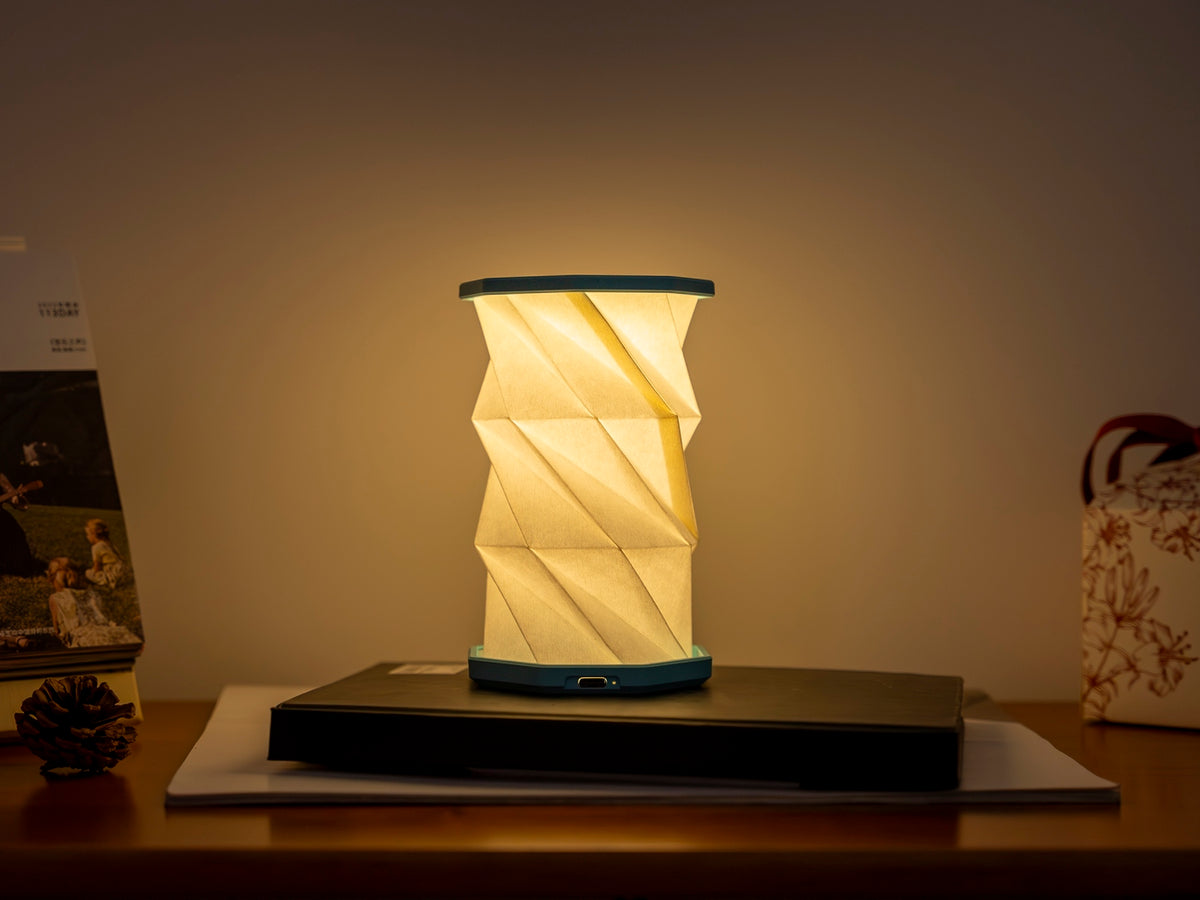 Gingko Design – Luz Twist Hexagon - Azul Laguna - Mini, lámpara de mesa plegable encendida, colocada sobre un mueble de madera