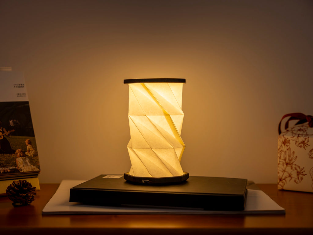 Gingko Design – Twist Hexagon Leuchte - Treibholz Walnuss - Mini, faltbare Tischleuchte eingeschaltet auf einem Holzschreibtisch