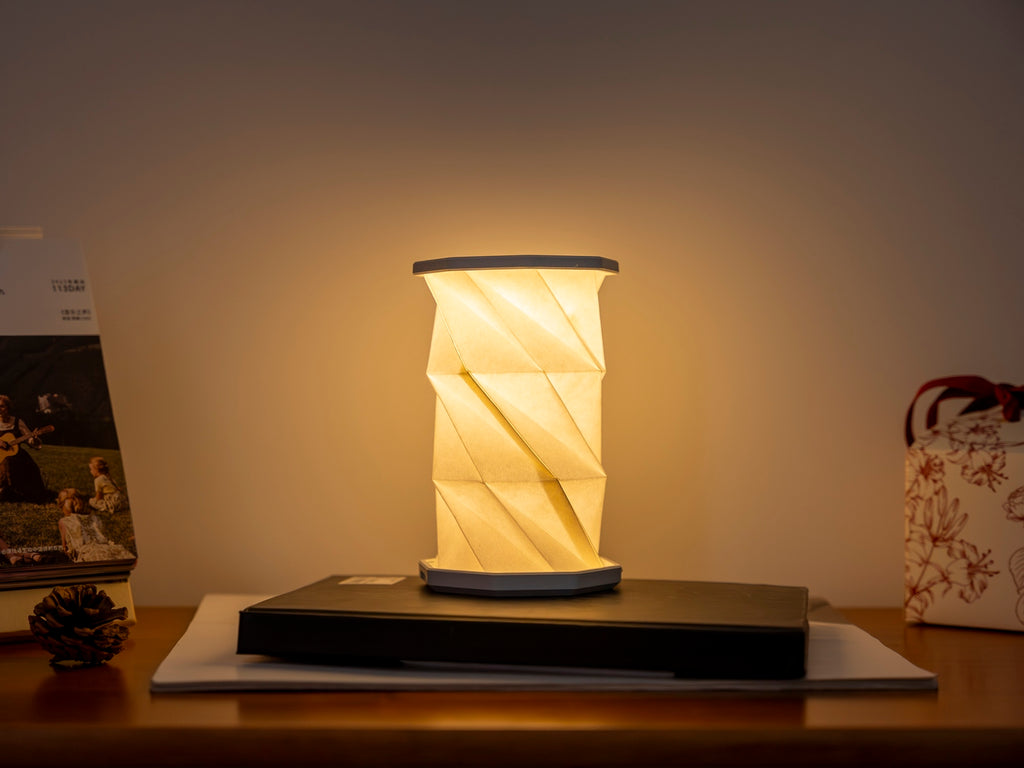 Gingko Design – Luz Twist Hexagon - Azul Laguna - Mini, lámpara de sobremesa plegable encendida, colocada sobre un escritorio de madera