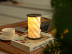 Gingko Design – Twist Hexagon Leuchte - Treibholz Walnuss - Mini, eingeschaltete Tischleuchte auf einem Buch, mit einer Tasse