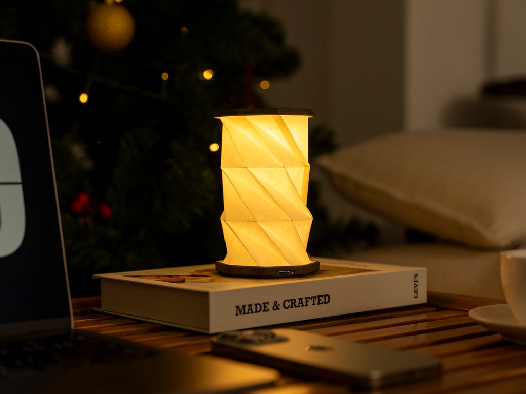 Gingko Design – Twist Hexagon Leuchte - Treibholz Walnuss - Mini, eingeschaltete Tischleuchte auf einem Buch, warme und gemütliche Atmosphäre