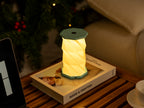 Gingko Design – Luz Twist Hexagon - Azul Laguna - Mini, lámpara de sobremesa plegable encendida sobre un libro, ambiente cálido