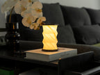 Gingko Design – Twist Hexagon Leuchte - Treibholz Walnuss - Mini, eingeschaltete Tischleuchte auf einem Buch in einem modernen Wohnzimmer