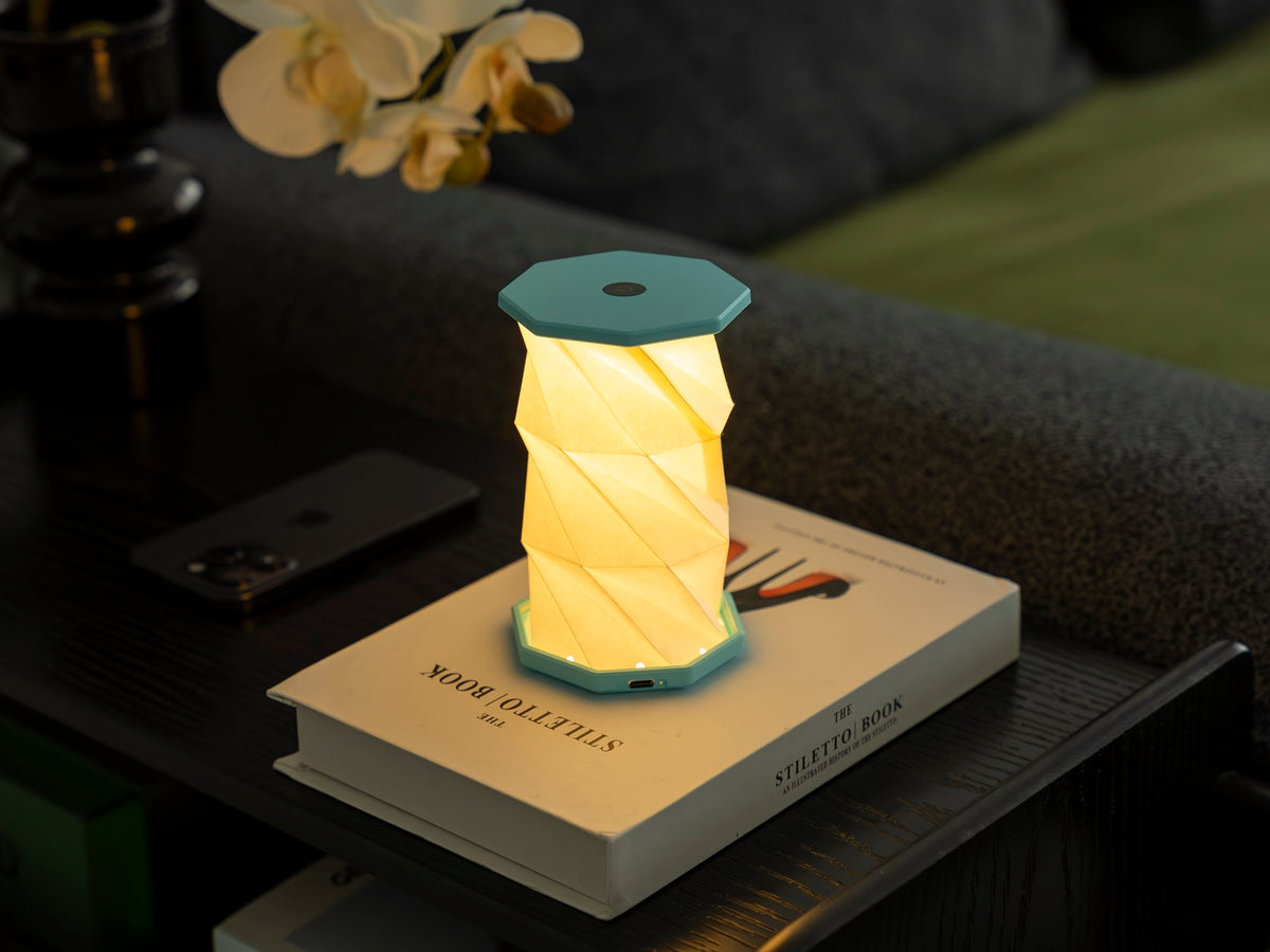 Gingko Design – Luz Twist Hexagon - Azul Laguna - Mini, lámpara de mesa plegable y luminosa colocada sobre un libro