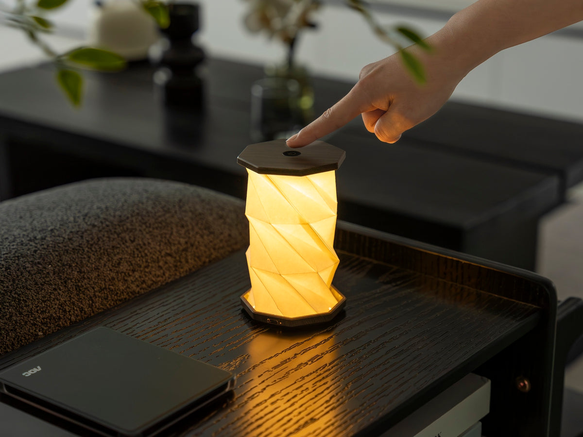 Gingko Design – Twist Hexagon Leuchte - Treibholz Walnuss - Mini, faltbare Tischleuchte aus Papier eingeschaltet auf einem Holztisch platziert