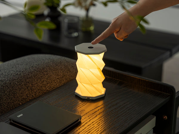 Gingko Design – Luz Twist Hexagon - Blanco Lunar - Mini, lámpara de mesa plegable encendida, colocada sobre una mesa de madera