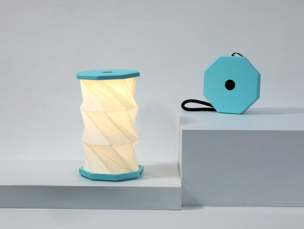 Gingko Design – Luz Twist Hexagon - Azul Laguna - Mini, lámpara plegable turquesa y blanca, colocada sobre una base blanca