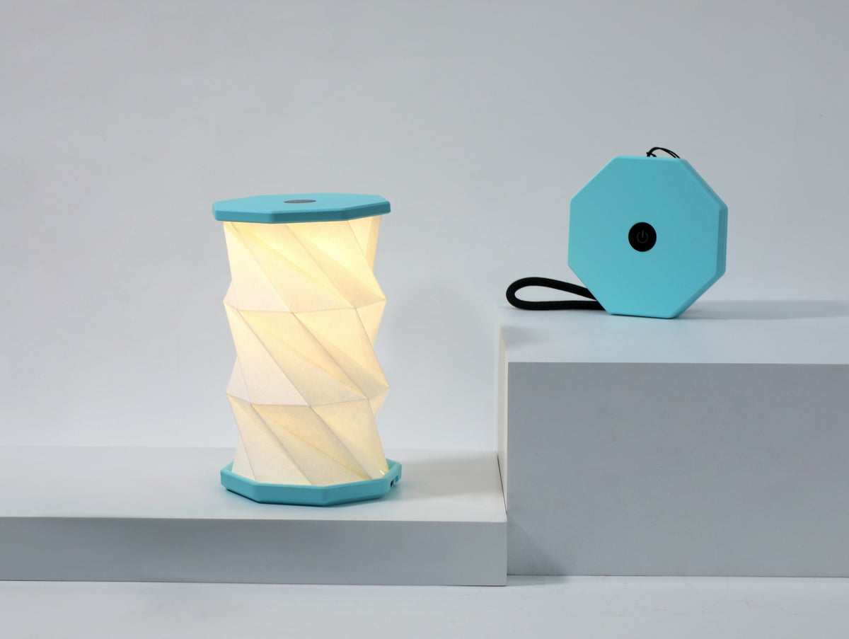 Gingko Design – Luz Twist Hexagon - Azul Laguna - Mini, lámpara plegable turquesa y blanca, colocada sobre una base blanca