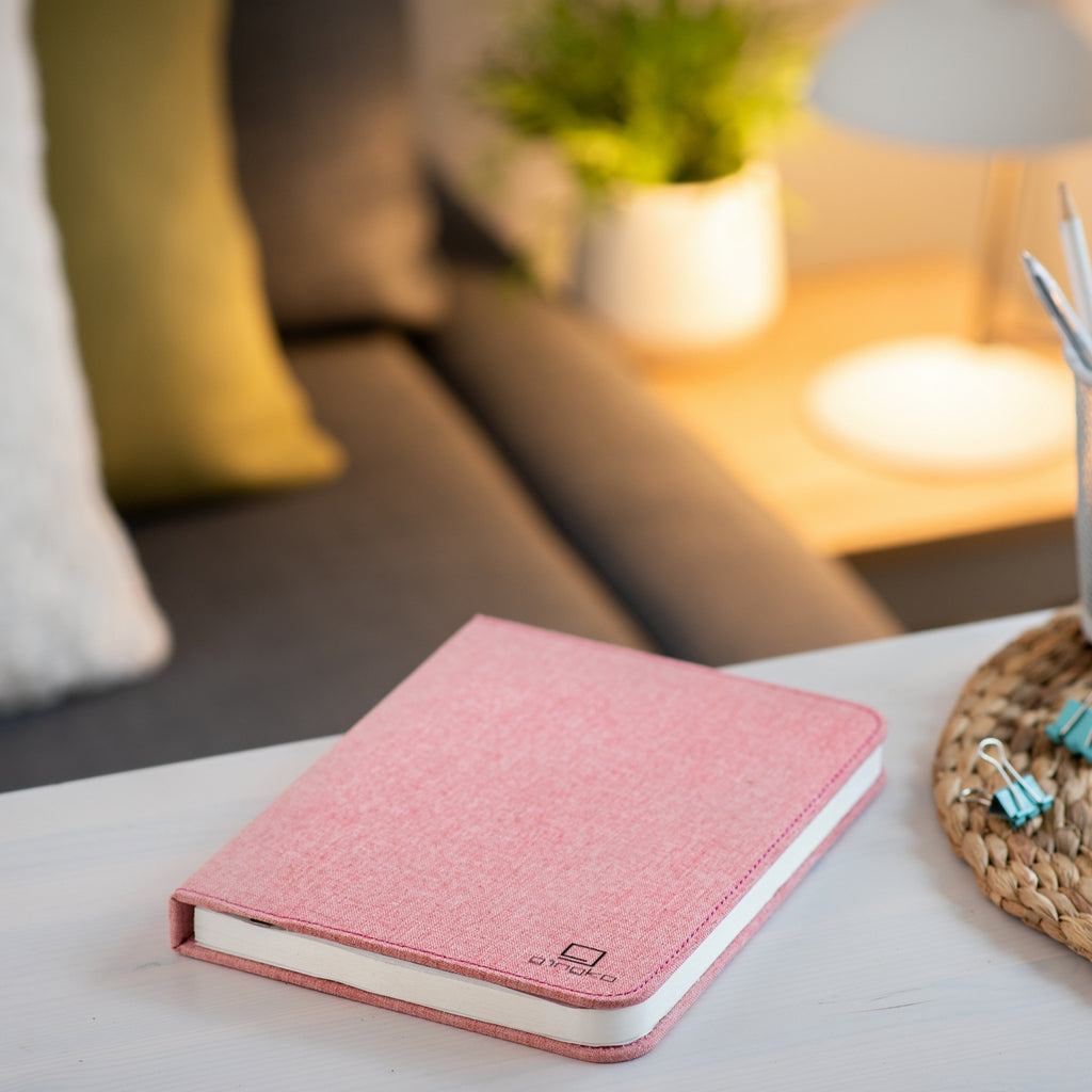 Gingko Design – Lampa Smart Book LED - Len Pudrowy Róż - 2 Rozmiary, różowy notes z tkaniny leżący na stoliku kawowym w salonie
