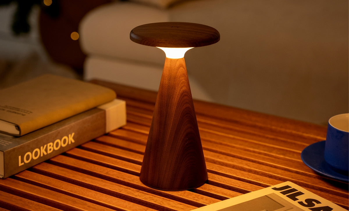 Gingko Design – Sylva Tischleuchte - Walnuss - 2 Größen, eingeschaltete braune Holztischleuchte auf einem Holztisch