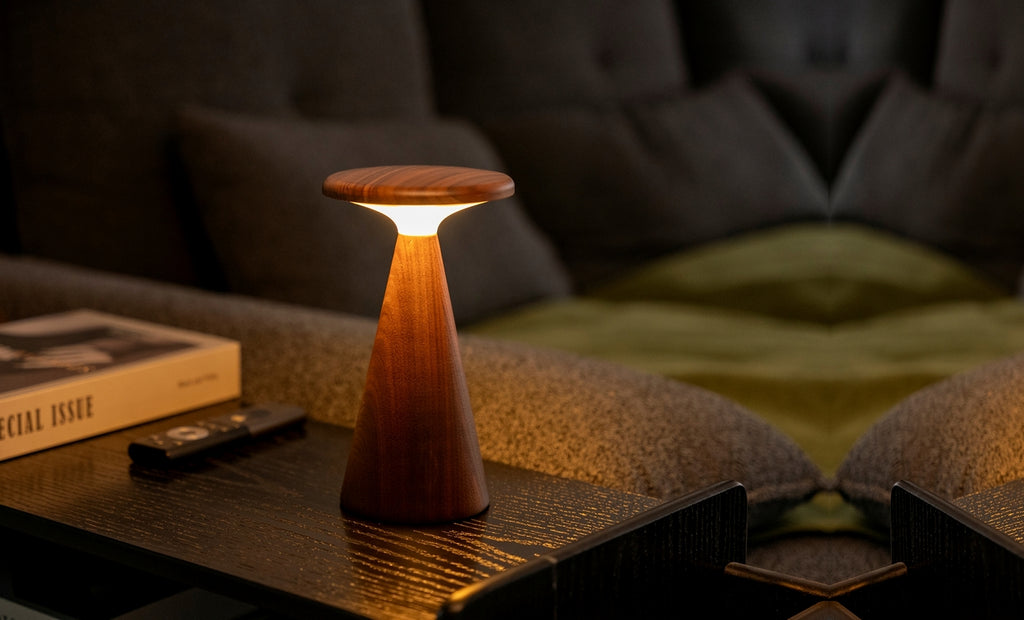 Gingko Design – Sylva Tischleuchte - Walnuss - 2 Größen, eingeschaltete Tischleuchte aus hellem Holz auf einem Couchtisch