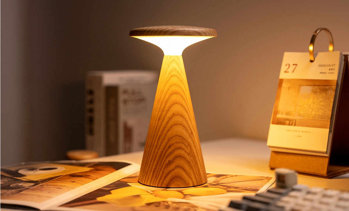 Gingko Design – Sylva Tischleuchte - Weiße Esche - 2 Größen, eingeschaltete Tischleuchte aus hellem Holz auf einem Schreibtisch