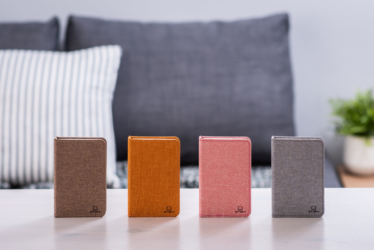 Gingko Design – Lámpara Smart Book LED - Lino Marrón Café - Mini, cuatro libretas de diferentes colores colocadas sobre una mesa de centro