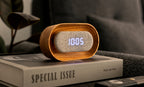 Gingko Design – Lumos Uhr - Oval Weiße Esche, Wecker aus hellem Holz und grauem Stoff auf einem Buch auf einem Nachttisch