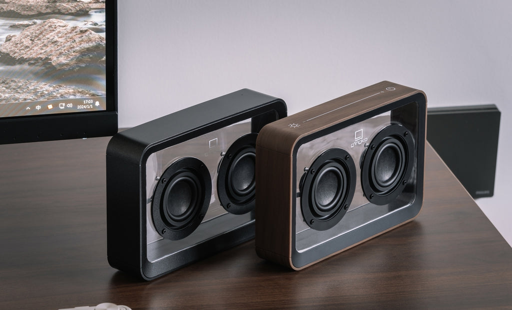 Gingko Design – Przezroczysty głośnik Bluetooth Mage – Orzech, dwa głośniki stojące na drewnianym biurku przed monitorem