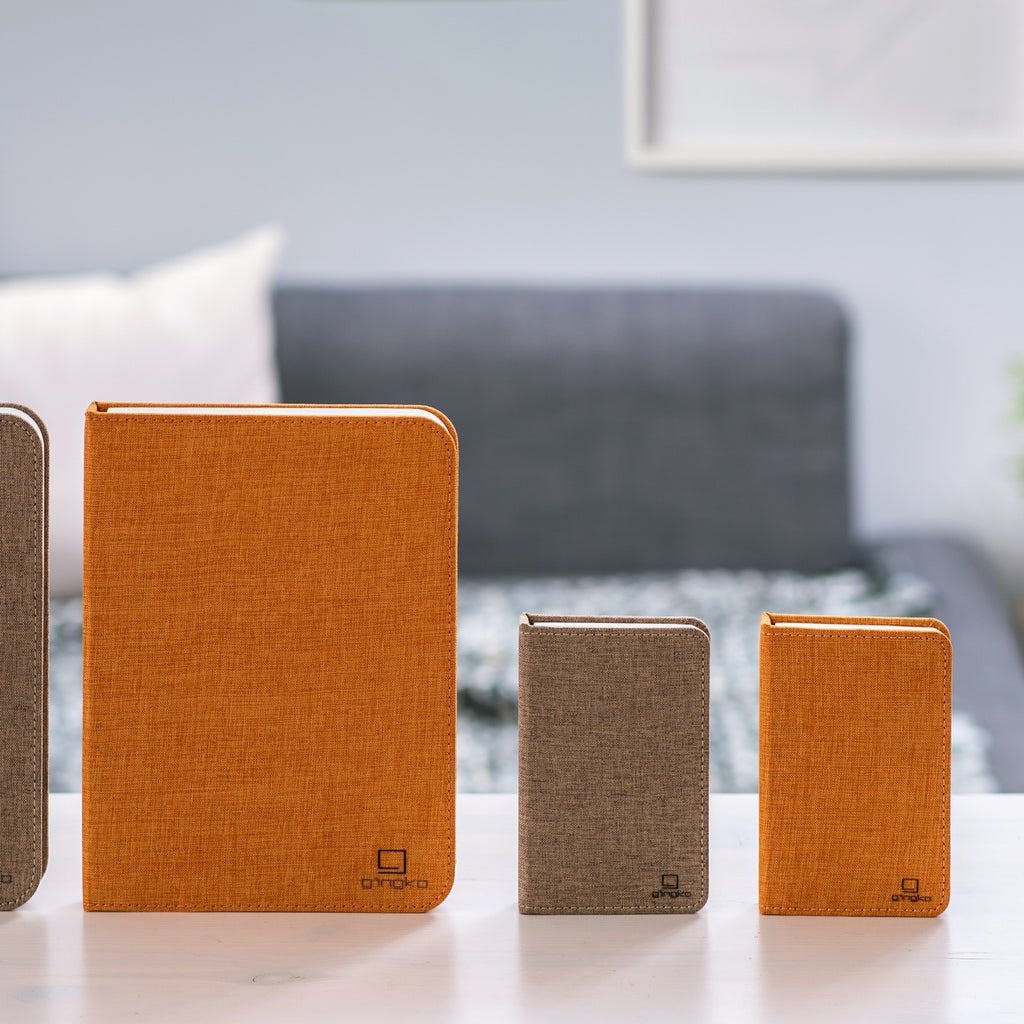 Gingko Design – Lámpara Smart Book LED - Lino Marrón Café - Mini, cuatro cuadernos de notas de diferentes tamaños y colores sobre una mesa