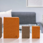 Gingko Design – Lámpara Smart Book LED - Lino Marrón Café - Mini, cuatro cuadernos de notas de diferentes tamaños y colores sobre una mesa