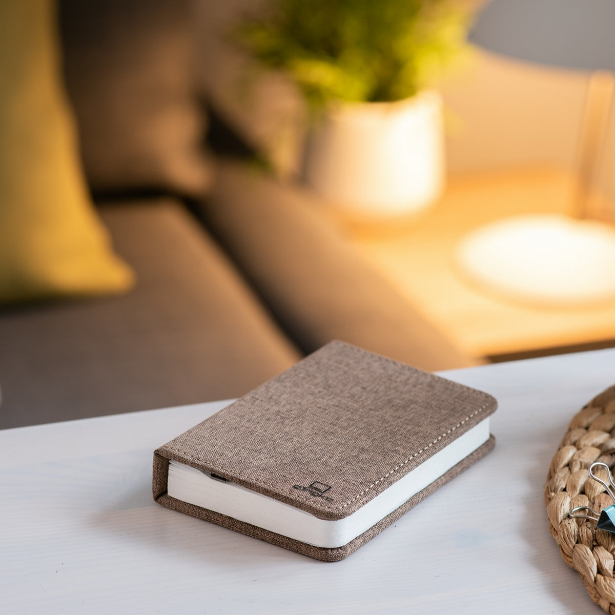 Gingko Design – Lámpara Smart Book LED - Lino Marrón Café - Mini, un cuaderno de notas marrón colocado sobre una mesa blanca en un salón
