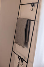 Handtuchleiter ESTINA mit einem handgewebten Handtuch und mehreren Haken an der Wand montiert.