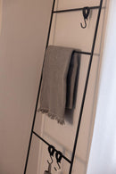 Handtuchleiter ESTINA mit einem handgewebten Handtuch und mehreren Haken an der Wand montiert.
