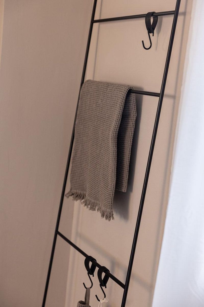 Handtuchleiter ESTINA mit einem handgewebten Handtuch und mehreren Haken an der Wand montiert.