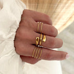 Instants Plaisirs – Bague "Lia" Acier, main de femme portant des bagues dorées, vue de côté, sur fond clair