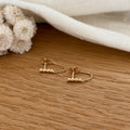 Instants Plaisirs – Boucles D'Oreilles Binta - Plaqué Or, boucles d'oreilles dorées avec chaînettes et perles sur un fond en bois