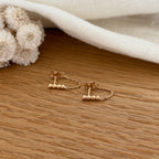 Instants Plaisirs – Boucles D'Oreilles Binta - Plaqué Or, boucles d'oreilles dorées avec chaînettes et perles sur un fond en bois