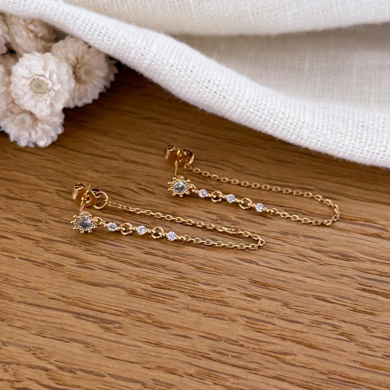 Instants Plaisirs – Boucles D'Oreilles "Chainy" Plaqué Or, boucles d'oreilles dorées avec chaînes et petits brillants sur bois clair