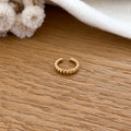 Instants Plaisirs – Bague D'Oreille Paz - Plaqué Or, bague dorée torsadée posée sur une table en bois clair