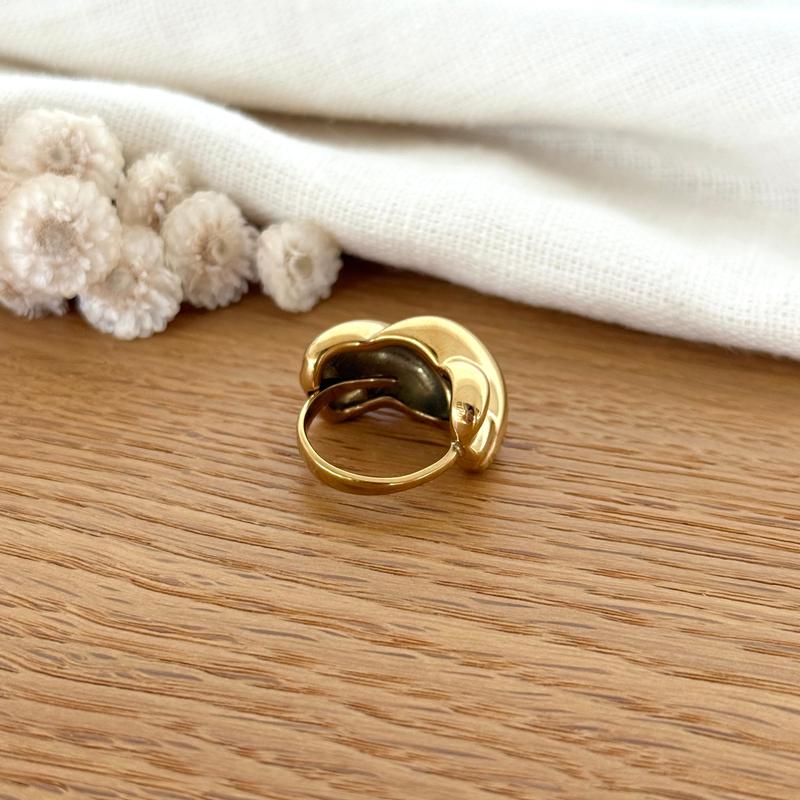 Instants Plaisirs – Bague "Abbie" Acier, bague dorée sur une table en bois avec un tissu blanc